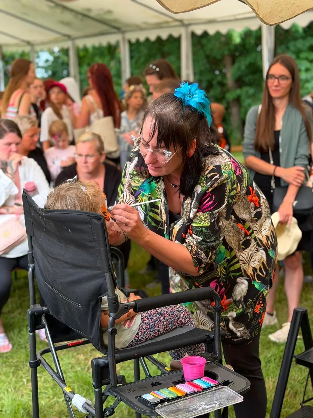 Claudia schminkt im Festzelt ein Kind, im Hintergrund wartende Familien