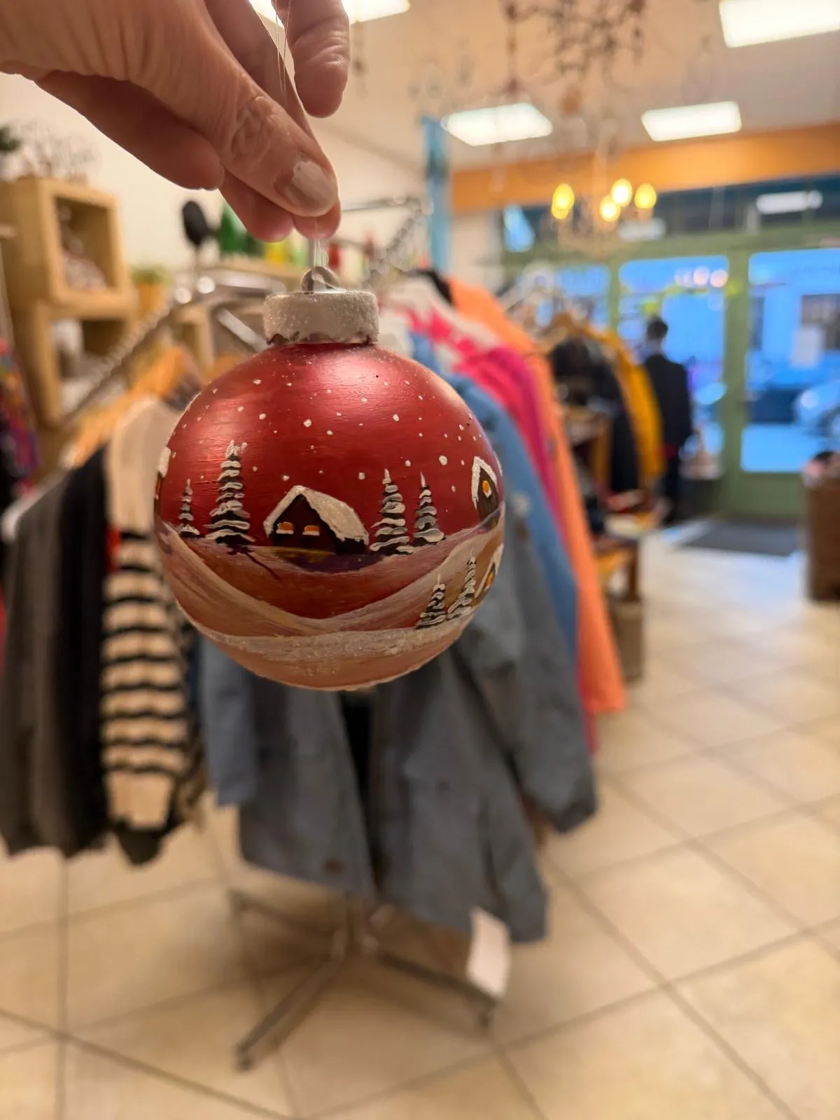 Rote Weihnachtskugel mit handgemaltem verschneitem Dorf und Tannen